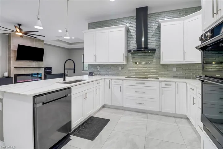 Kitchen with ceiling fan, kitchen peninsula, pendant lighting, wall chimney range hood, and black appliances