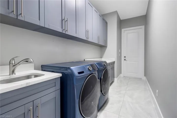 Clothes washing area featuring sink, light tile patterned floors, cabinets, and washing machine and clothes dryer