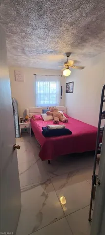 Bedroom featuring a textured ceiling, light marble finish flooring, and a ceiling fan