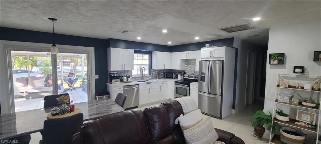 Kitchen with stainless steel appliances, light countertops, white cabinets, decorative backsplash, and decorative light fixtures