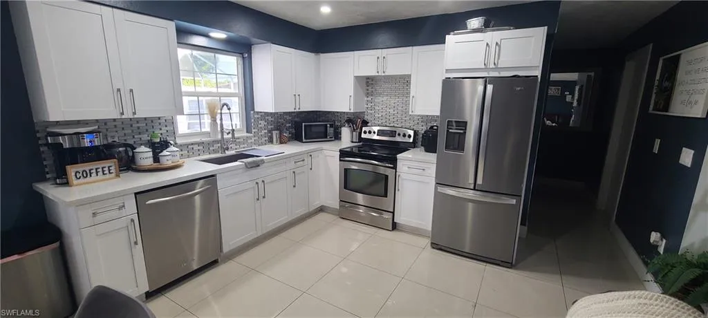 Kitchen featuring stainless steel appliances, white cabinetry, light tile patterned floors, decorative backsplash, and light stone counters
