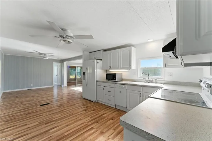 Kitchen with white appliances, ventilation hood, light wood-style floors, a ceiling fan, and light countertops