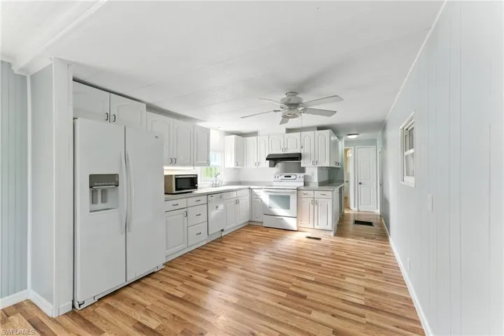 Kitchen featuring white appliances, under cabinet range hood, light wood-style flooring, a ceiling fan, and white cabinetry