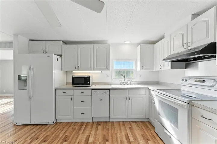 Kitchen featuring white appliances, under cabinet range hood, light wood-type flooring, and white cabinetry