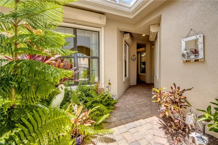 Entryway featuring a paver stone walkway, stucco exterior, and lush tropical landscaping