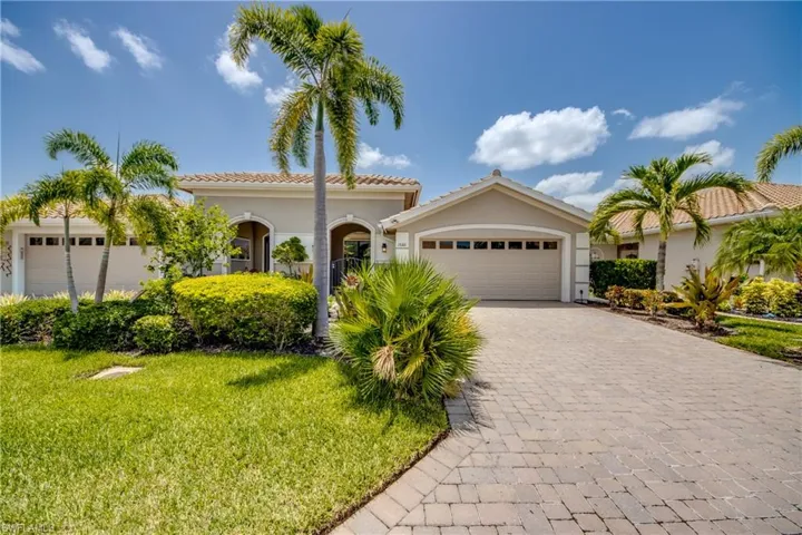Property exterior featuring a paver driveway, lush green lawn, mature palm trees, and manicured shrubbery