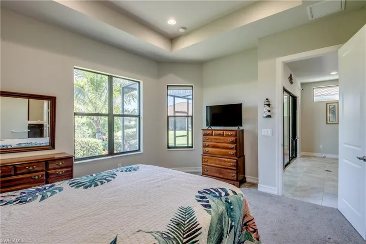 Recessed lighting and a tray ceiling accent this carpeted room, featuring multiple windows with outdoor landscaping visible