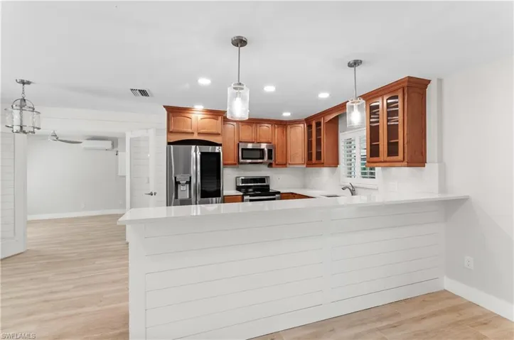 Kitchen featuring hanging light fixtures, glass insert cabinets, a peninsula, light wood finished floors, and stainless steel appliances