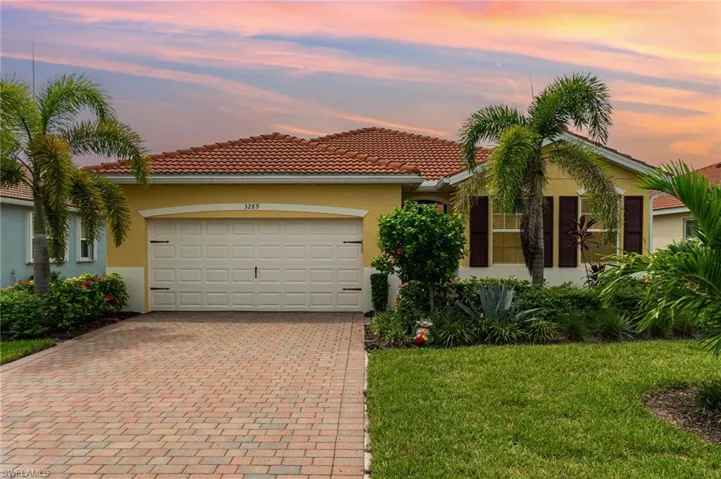 View of front facade featuring stucco siding, an attached garage, a tiled roof, decorative driveway, and a front yard