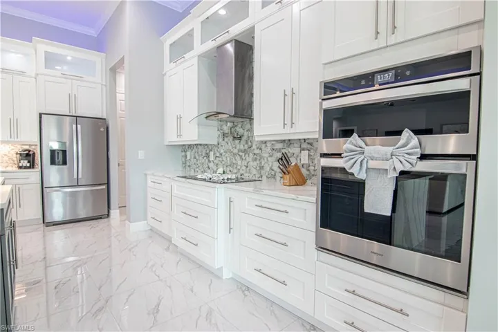 Kitchen featuring backsplash, appliances with stainless steel finishes, wall chimney range hood, and white cabinetry