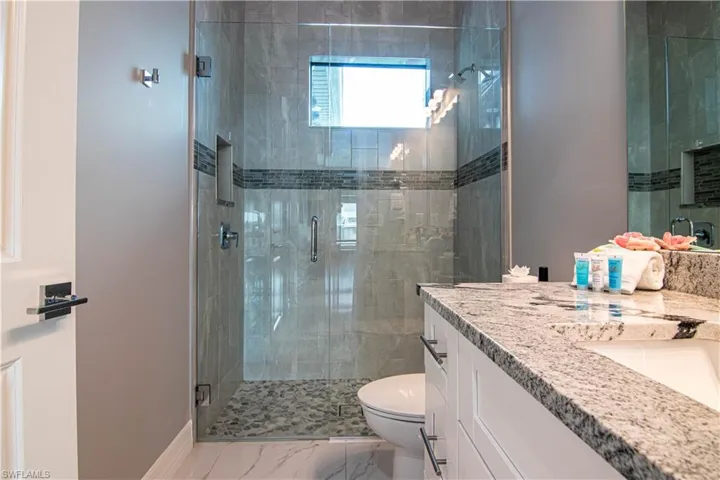 Bathroom featuring a shower with door, toilet, and vanity