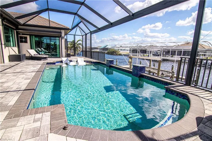 View of pool featuring a water view, a patio area, a dock, and glass enclosure