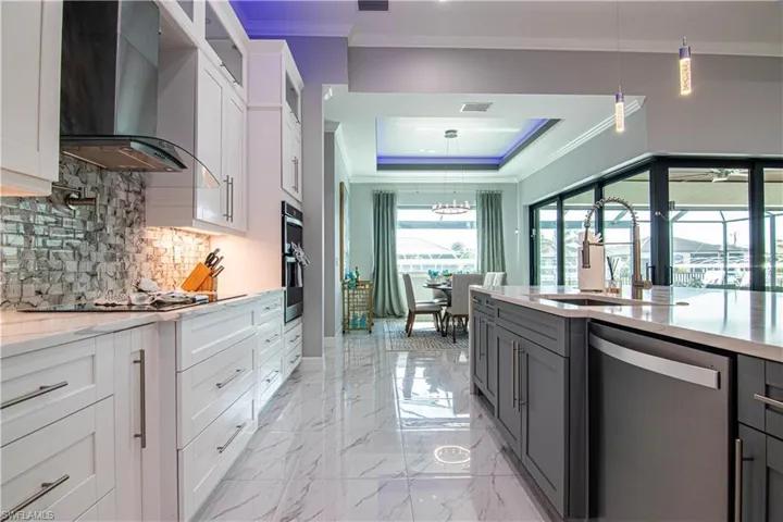 Kitchen featuring white cabinetry, stainless steel appliances, decorative light fixtures, wall chimney range hood, and sink