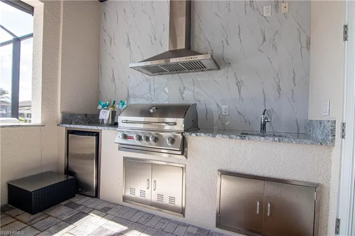 Kitchen featuring sink, wall chimney exhaust hood, stainless steel fridge, and stone countertops