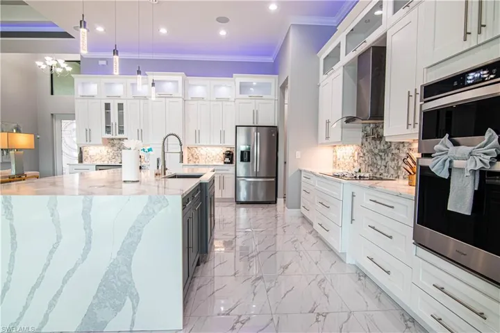 Kitchen featuring sink, hanging light fixtures, stainless steel appliances, white cabinets, and wall chimney exhaust hood