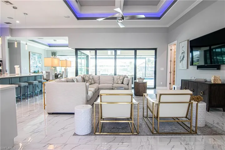Living room with ceiling fan, a tray ceiling, and ornamental molding