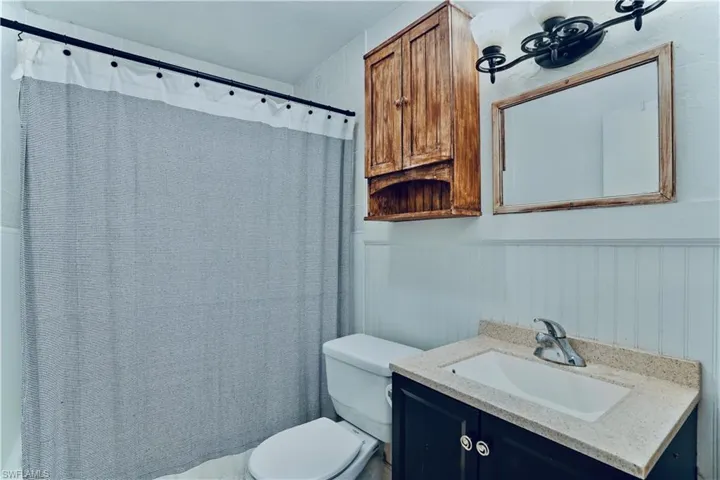 Full bath with toilet, vanity, wainscoting, and a shower with curtain