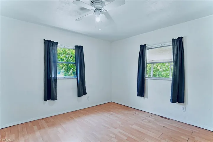Unfurnished room featuring plenty of natural light, wood finished floors, ceiling fan, and baseboards