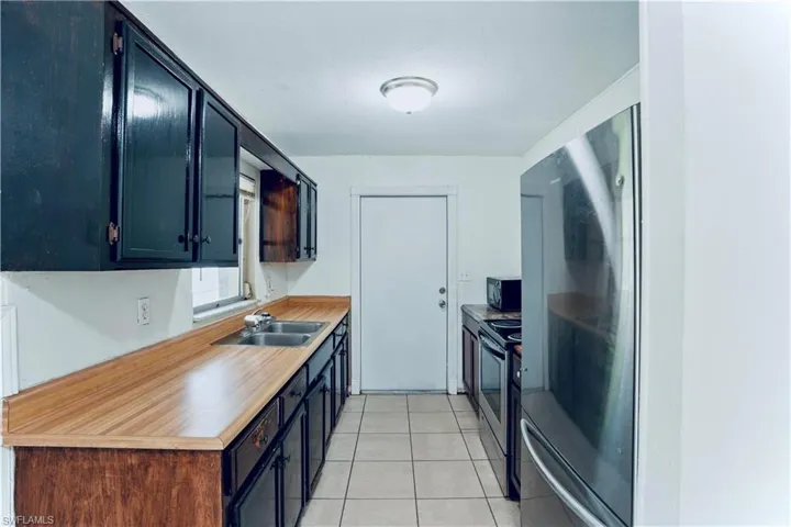 Kitchen with a sink, black microwave, electric range, light tile patterned floors, and light countertops