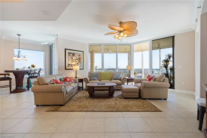 Living room with a wall of windows, crown molding, healthy amount of natural light, a ceiling fan, and light tile patterned flooring