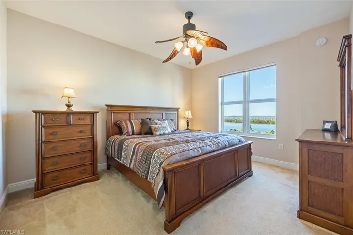 Bedroom with light colored carpet, ceiling fan, and a water view