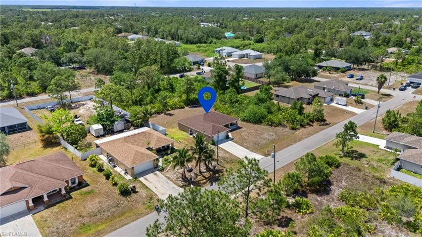 Aerial view of property and surrounding area featuring nearby suburban area and a heavily wooded area