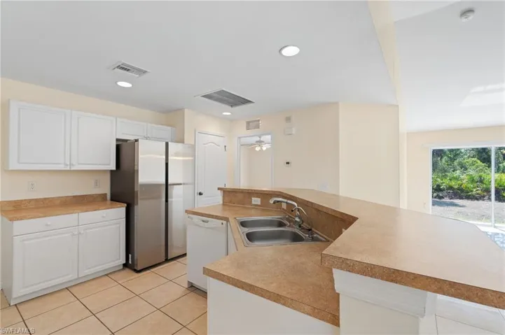 Kitchen with an island with sink, freestanding refrigerator, white dishwasher, light countertops, and recessed lighting