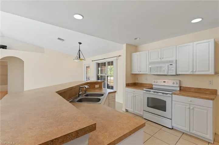 Kitchen featuring white appliances, a spacious island, arched walkways, white cabinets, and light tile patterned floors