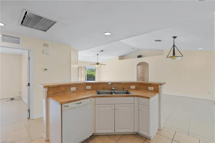 Kitchen with a kitchen island with sink, white cabinetry, dishwasher, light countertops, and arched walkways
