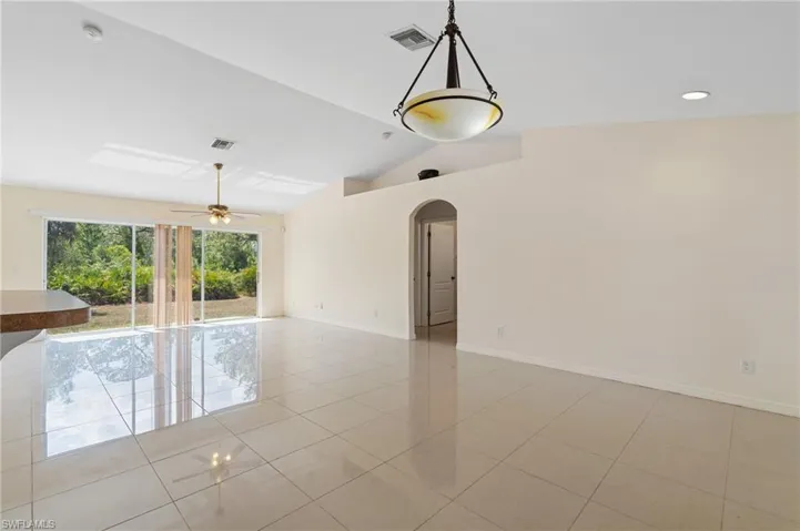Empty room featuring arched walkways, lofted ceiling, light tile patterned floors, and ceiling fan