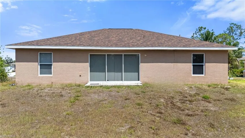 Back of house with roof with shingles, stucco siding, and a yard