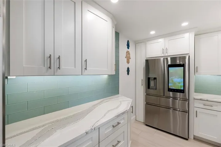 Kitchen featuring white cabinetry, stainless steel fridge with ice dispenser, tasteful backsplash, and light stone counters