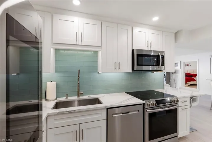 Kitchen featuring white cabinetry, stainless steel appliances, light stone counters, sink, and tasteful backsplash