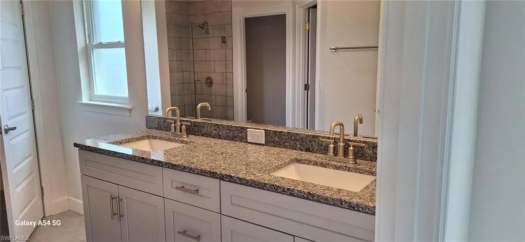 Bathroom featuring a shower stall, double vanity, a sink, and tile patterned floors