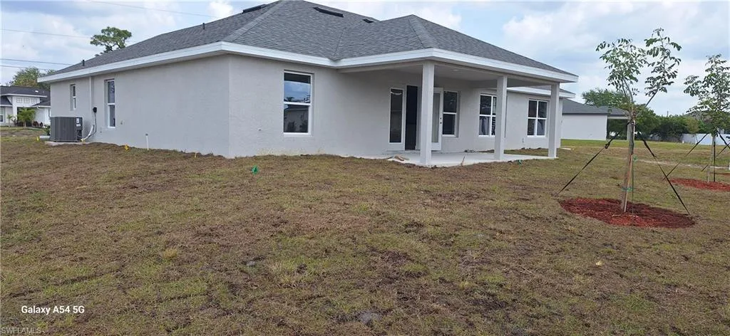 Rear view of property featuring stucco siding, cooling unit, a patio, and roof with shingles