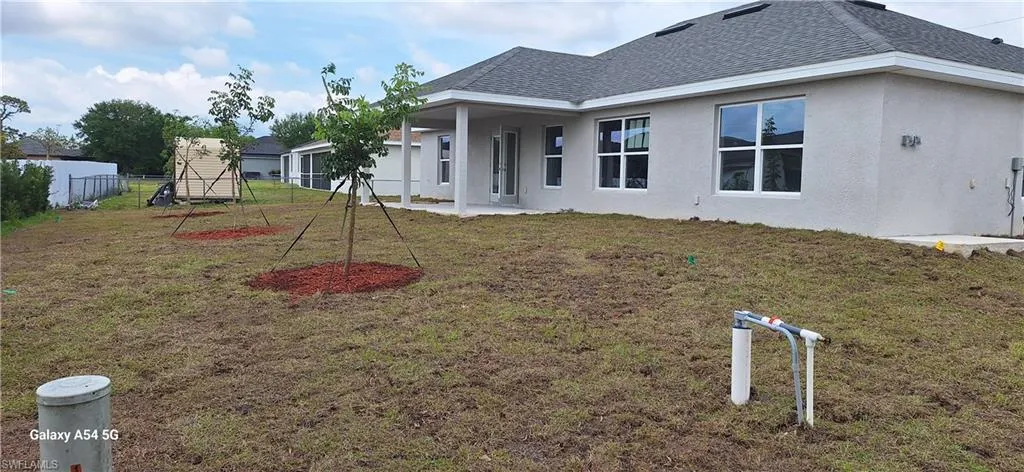 Back of house featuring stucco siding, fence, a lawn, and roof with shingles