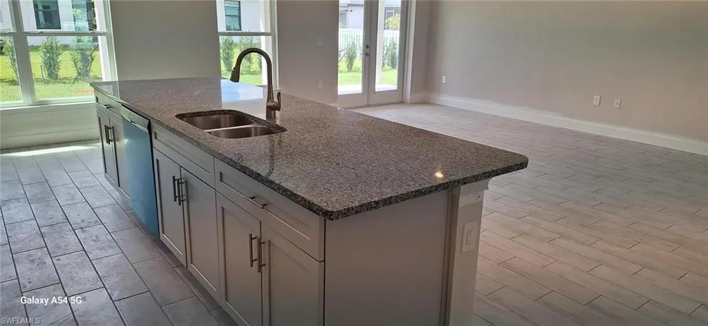 Kitchen with dark stone countertops, a sink, dishwasher, a kitchen island with sink, and wood tiled floor
