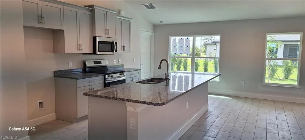 Kitchen with a sink, appliances with stainless steel finishes, wood tiled floor, visible vents, and dark stone counters