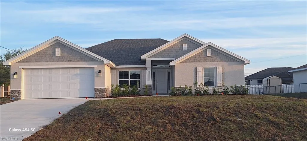 View of front of house with a front lawn, fence, driveway, stone siding, and an attached garage