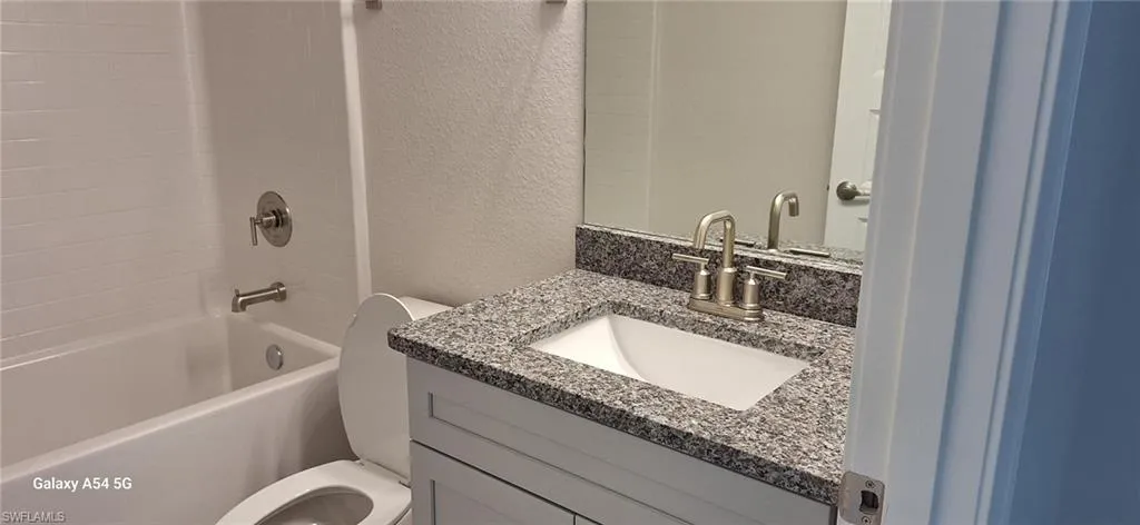 Full bathroom featuring a textured wall, toilet, vanity, and washtub / shower combination
