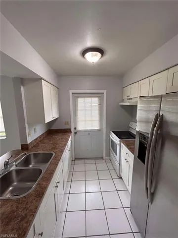 Kitchen featuring stainless steel fridge with ice dispenser, white cabinetry, electric stove, light tile patterned flooring, and dark countertops