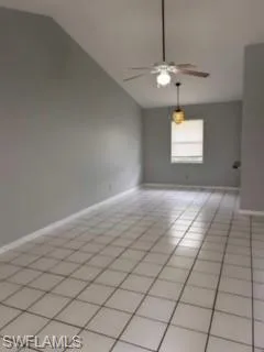 Empty room with light tile patterned floors, lofted ceiling, and ceiling fan