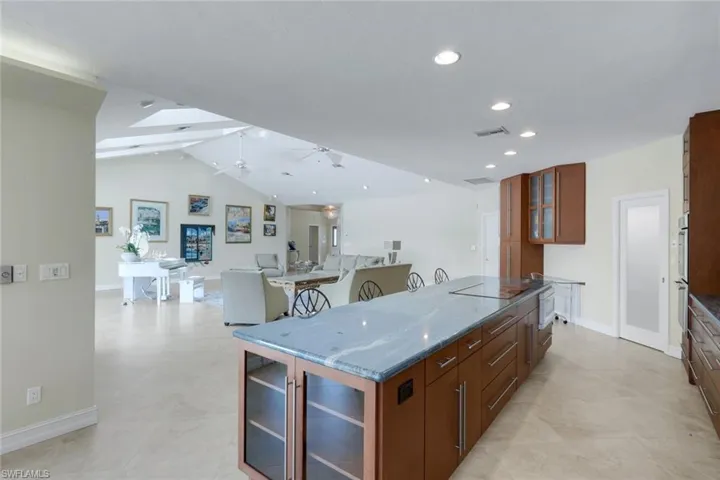 Kitchen with glass fronted cabinets, open floor plan, dark stone counters, wood finish cabinets, and vaulted ceiling