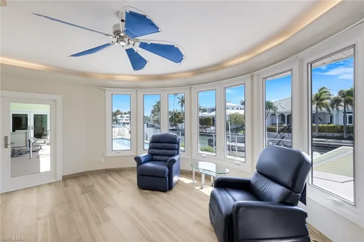 Living area with light wood finished floors, healthy amount of natural light, ceiling fan, and a tray ceiling