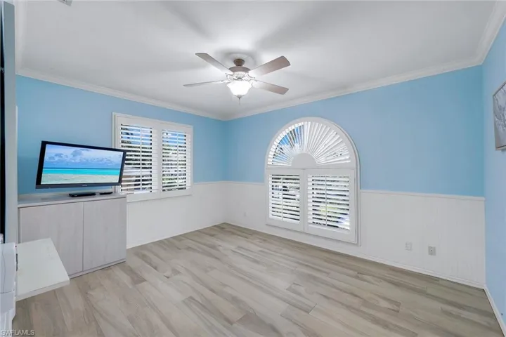 Unfurnished room with a wainscoted wall, ceiling fan, light wood finished floors, and crown molding