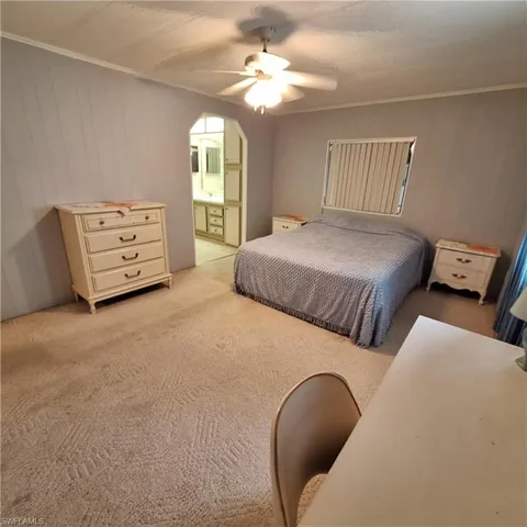 Bedroom with ornamental molding, light carpet, ceiling fan, and ensuite bathroom