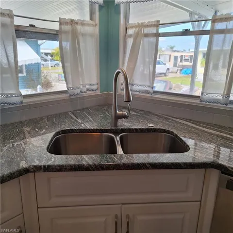 Kitchen with stainless steel dishwasher, dark stone counters, sink, and white cabinets