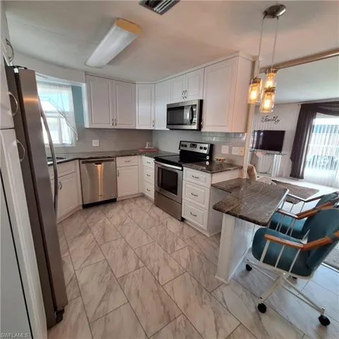 Kitchen featuring white cabinetry, hanging light fixtures, stainless steel appliances, and a healthy amount of sunlight