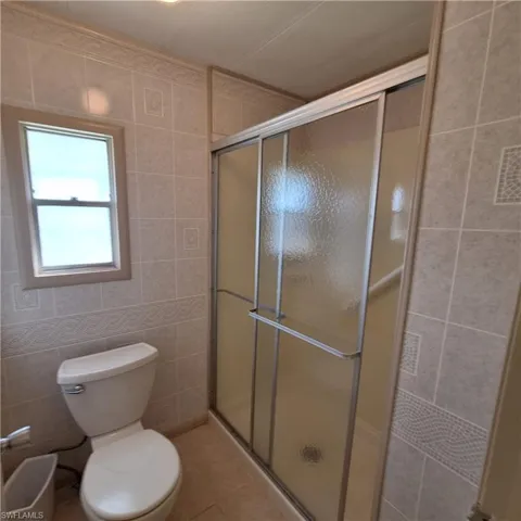 Bathroom featuring tile patterned floors, toilet, a shower with shower door, and tile walls