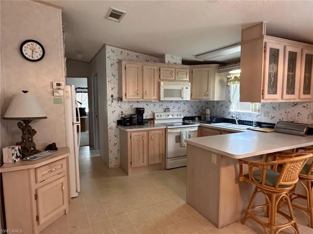 Kitchen with white appliances, light countertops, lofted ceiling, a peninsula, and glass insert cabinets